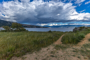 Green grass in a clearing, rest on a trail near the town of Baska, view of the bay and the city panorama