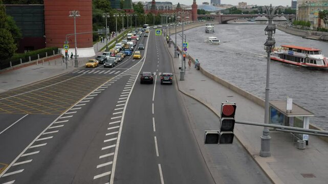 The perspective from the bridge onto a bustling thoroughfare, with a plethora of automobiles, trucks, and buses, alongside a river where a vessel is navigating.