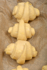 An overhead close-up of several raw, rolled croissant dough pieces arranged on parchment paper before baking