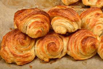 A close-up shot shows a cluster of homemade golden-brown, freshly baked croissants with visible layers and a flaky texture, resting on a sheet of parchment paper