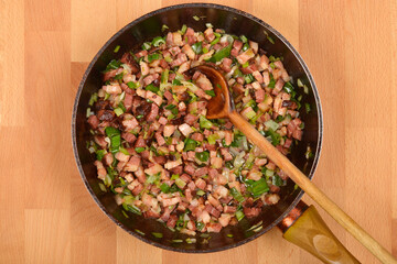 A top-down view shows diced pancetta and chopped green onions being stirred in a dark skillet with a wooden spoon