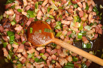 A close-up overhead shot shows diced pancetta and chopped green onions being stirred with a wooden...