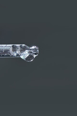 Close-up of transparent glass pipette against plain gray background with liquid droplets inside.