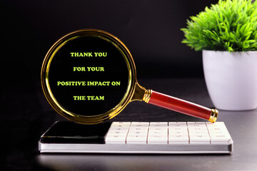 A magnifying glass displays a thank you message for positive contributions to the team, placed on a...