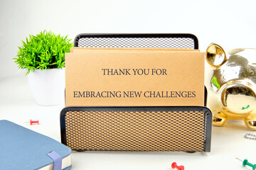 A note expressing gratitude for facing new challenges is placed on a stylish desk organizer, accompanied by a small plant and a decorative piggy bank