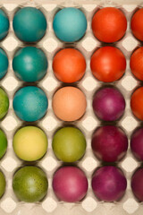 A vertical top-down shot showcases a full carton of vibrantly colored Easter eggs in shades of blue, green, yellow, orange, red, and purple