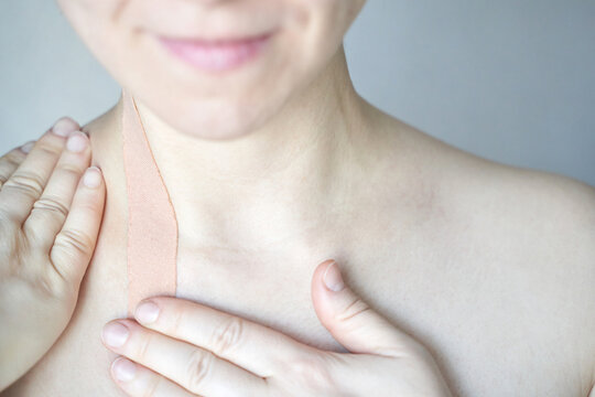 Female adult caucasian applying therapeutic kinesiology tape to shoulder neck area for pain relief.