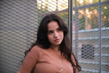 Portrait of a young latin woman with long brown hair wearing a brown shirt standing near a metallic...