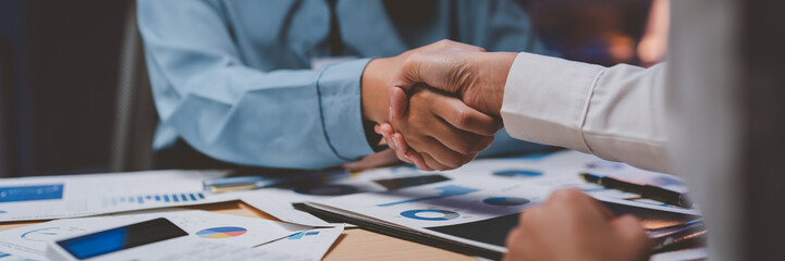 Business people shaking hands after discussing financial charts and graphs late at night
