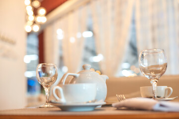 Elegant table setting with white teapot and glassware in cozy cafe ambiance.