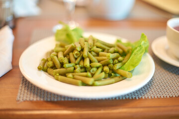 Delicious cooked green beans on white plate with lettuce garnish in warm dining setting.