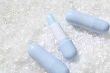 Moisturizing lip balms on artificial snow, flat lay. Space for text
