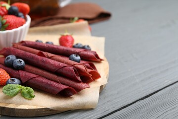 Tasty fruit leather rolls, strawberries, blueberries and mint on grey wooden table, closeup. Space...