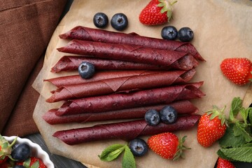 Tasty fruit leather rolls, strawberries, blueberries and mint on grey wooden table, flat lay