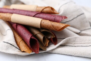 Tasty fruit leather rolls on white tiled table, closeup