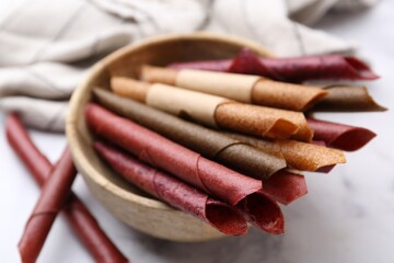 Tasty fruit leather rolls on white marble table, closeup