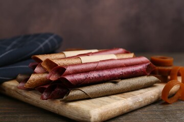 Tasty fruit leather rolls on wooden table, closeup