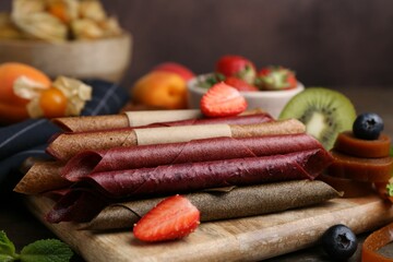 Tasty candied leather rolls, fruits and berries on wooden table, closeup