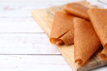 Delicious fruit leather rolls on white wooden table, closeup. Space for text