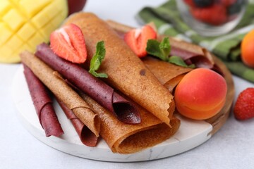 Delicious fruit leather rolls, mint, apricot, mango and strawberry on light table, closeup