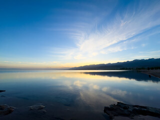 Fototapeta premium Quiet mountain lake, evening light on the water, Kyrgyzstan. Still water and mountain reflection in the lake.