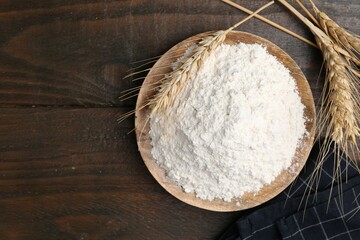 Wheat flour and spikes on wooden table, flat lay. Space for text