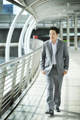 Asian businessman walking on a bridge outside office background	