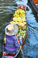 A vendor is rowing a boat to sell fruit in a canal at Damnoen Saduak Floating Market, the most famous floating market in Thailand.