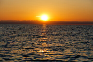 The sun is setting over the ocean, casting a warm glow on the water