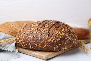 Fresh bread loaves and spikes on white tiled table, closeup