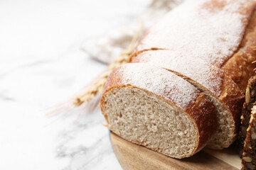 Freshly baked loaf of bread and spike on white marble table, closeup. Space for text