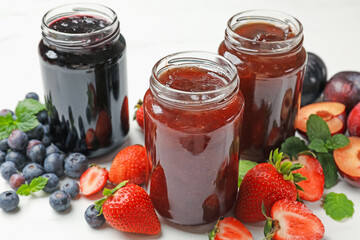 Different sweet jams in jars and ingredients on white table, closeup