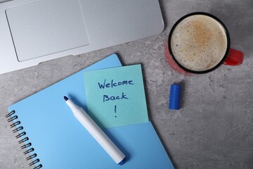Sticky note with phrase Welcome Back, laptop, coffee, marker and notebook on grey table, flat lay