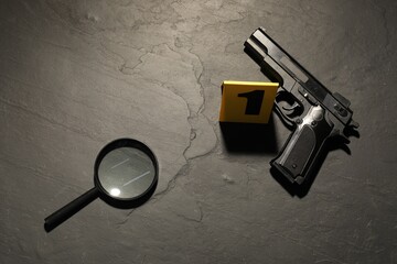 Forensic expertise. Crime scene with gun and magnifying glass on grey background, flat lay