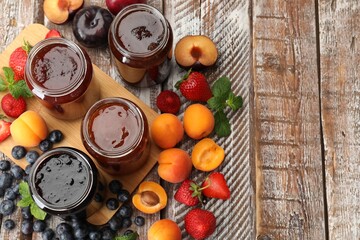 Different jams in jars and ingredients on wooden table, flat lay. Space for text