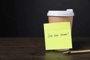 Paper note with phrase Join Our Team, pen and cup of coffee on wooden table. Space for text