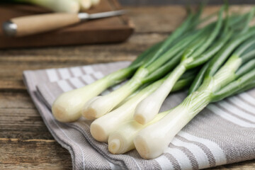 Fresh ripe green onions and towel on wooden table, closeup