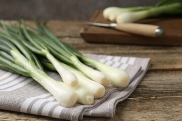 Fresh ripe green onions and towel on wooden table, closeup