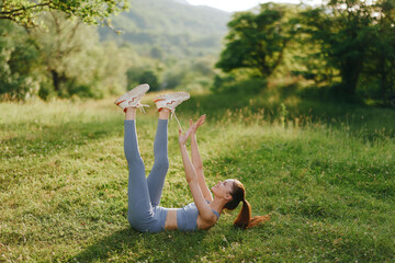Young woman exercising outdoors in the summer, practicing leg raises in a lush green field,...