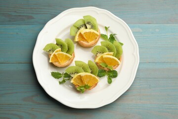 Tartlets with fruits and mint on light blue wooden table, top view. Delicious dessert