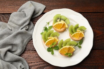 Tartlets with fruits and mint on wooden table, top view. Delicious dessert