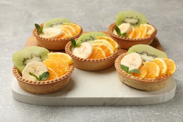 Tartlets with fruits and mint on gray textured table, closeup. Delicious dessert