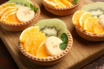 Tartlets with fruits and mint on table, closeup. Delicious dessert