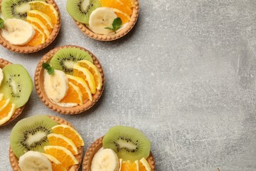 Delicious dessert. Tartlets with fruits and mint on gray textured table, flat lay. Space for text