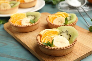 Tartlets with fruits and mint on light blue wooden table, closeup. Delicious dessert