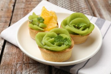 Tartlets with fruits and mint on wooden table, closeup. Delicious dessert