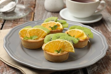 Tartlets with fruits and mint on wooden table, closeup. Delicious dessert