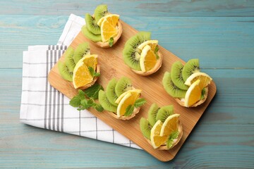 Tartlets with fruits and mint on light blue wooden table, top view. Delicious dessert