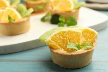 Tartlets with fruits and mint on light blue wooden table, closeup. Delicious dessert