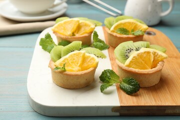 Tartlets with fruits and mint on light blue wooden table, closeup. Delicious dessert